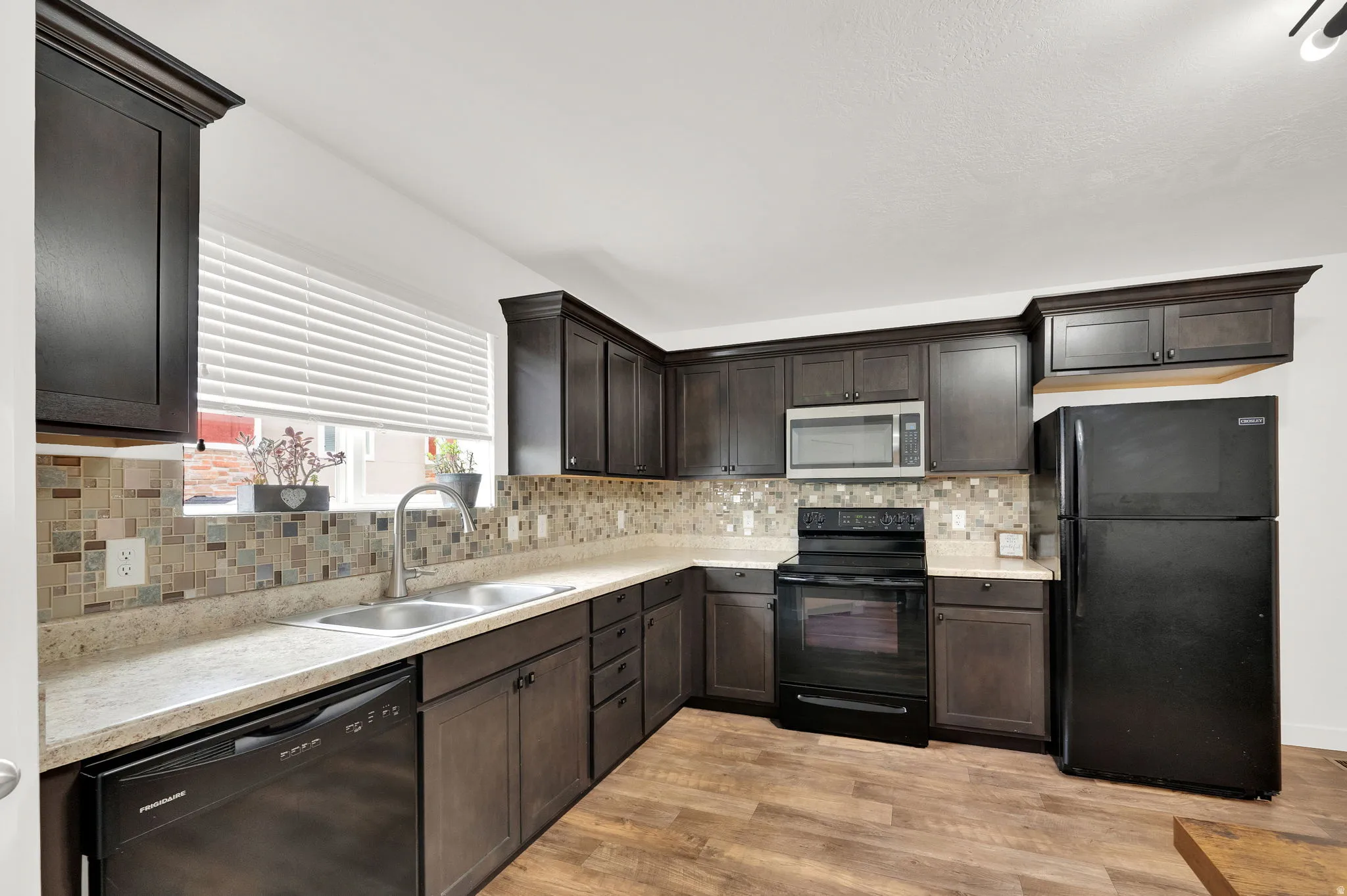 Kitchen featuring dark wood-finish cabinetry, light countertops, mosaic tile backsplash, stainless steel microwave, and wood-finish flooring