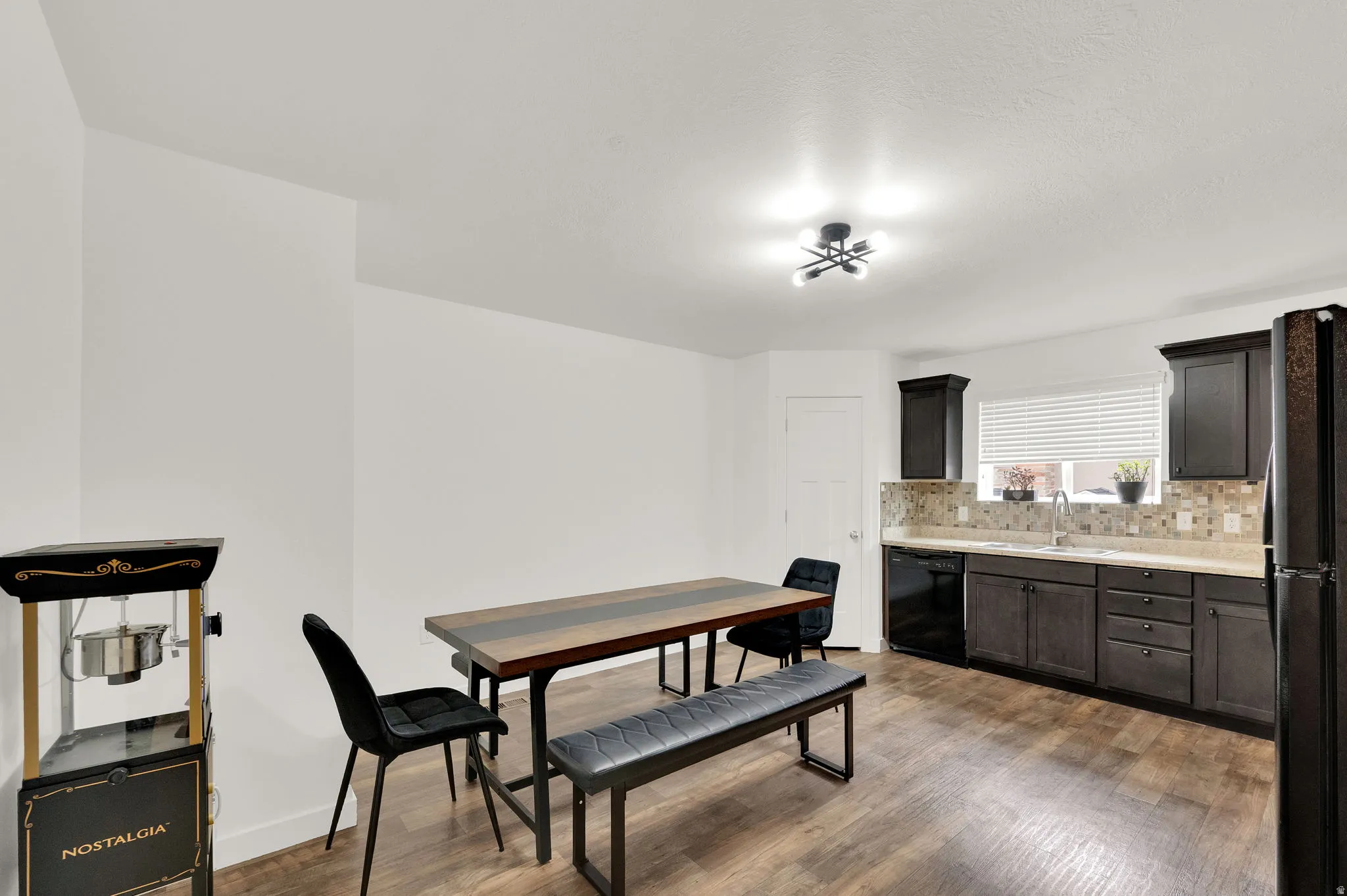 Kitchen and dining area featuring dark wood-finish cabinetry, light-toned countertops, a mosaic tile backsplash, and wood-finish flooring
