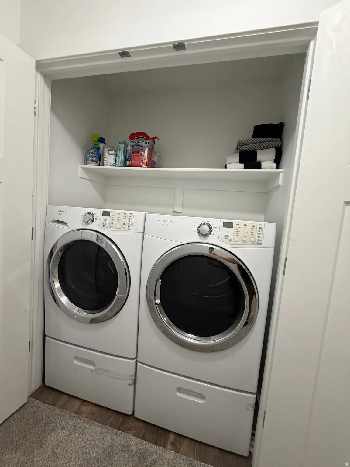 Dedicated laundry area featuring front-loading appliances, a built-in storage shelf, and wood-finish flooring
