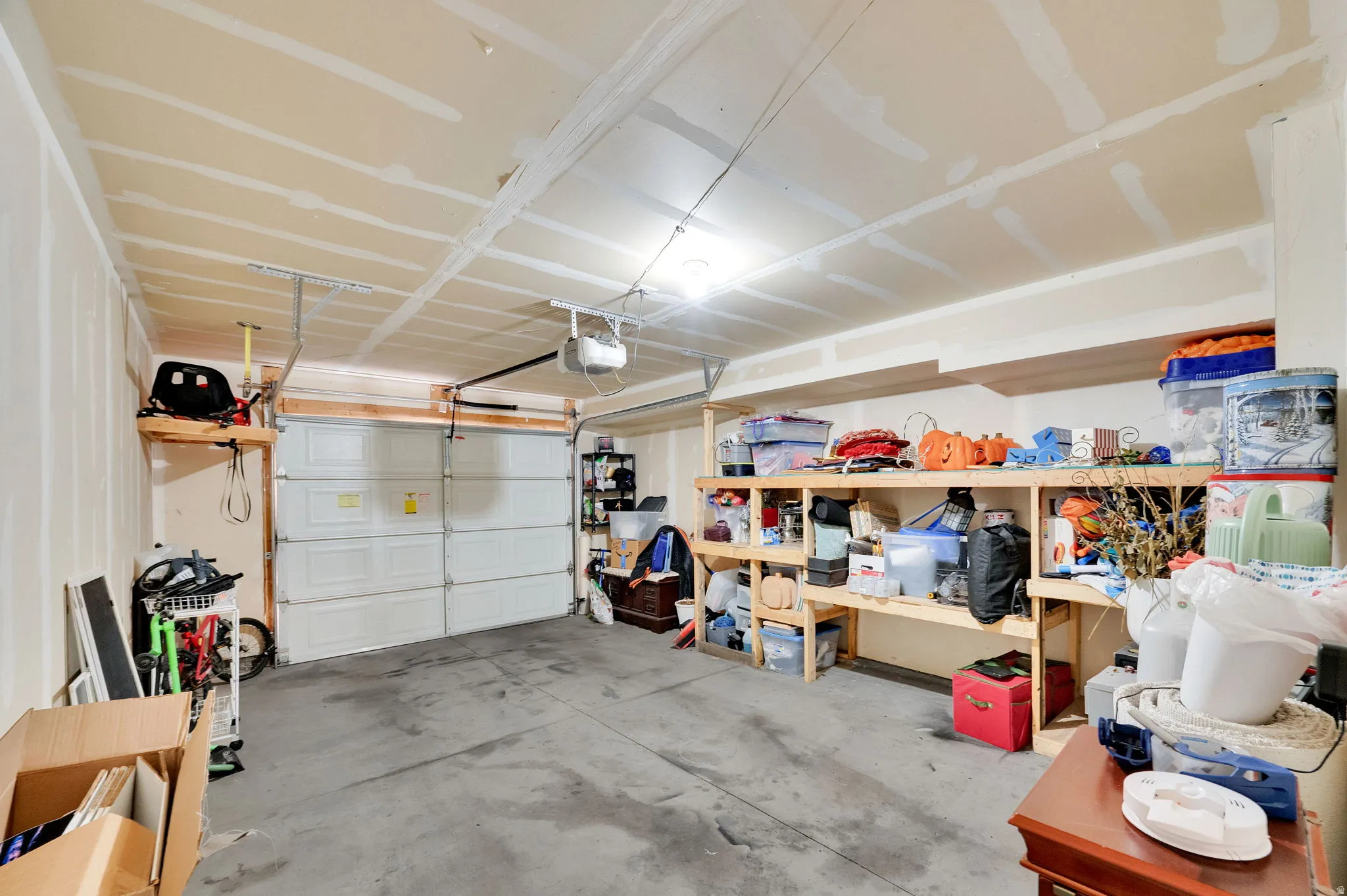 Spacious garage with overhead lighting, a garage door opener, and a concrete floor