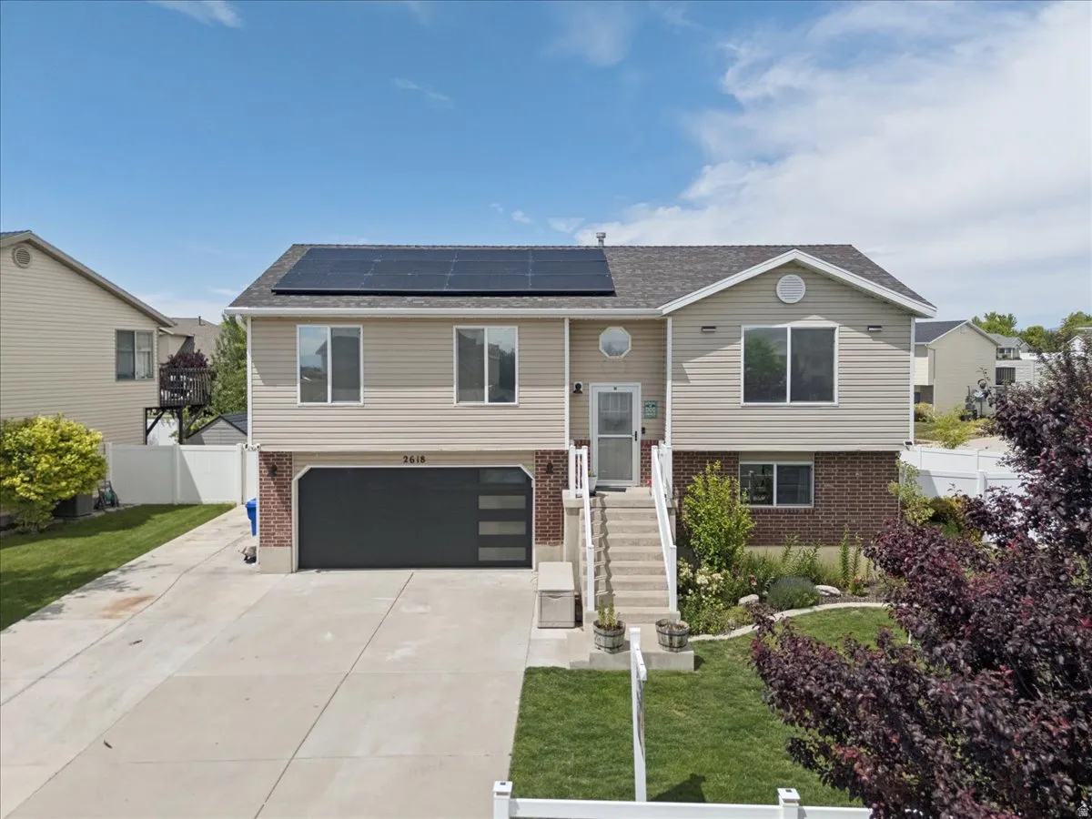 Split-level residence featuring a two-car garage with modern frosted glass panels, an extended concrete driveway, and solar panels