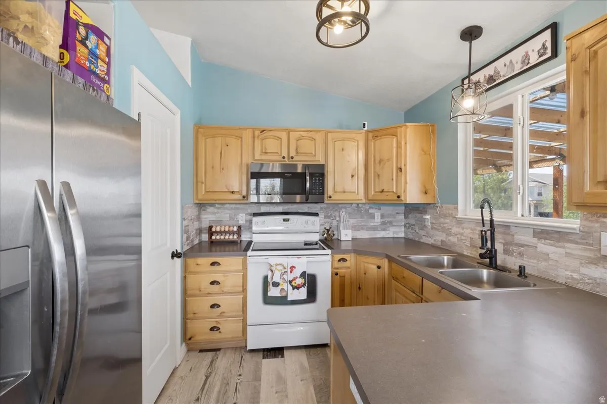 Kitchen featuring light wood cabinetry, stone-look backsplash, and dark countertops