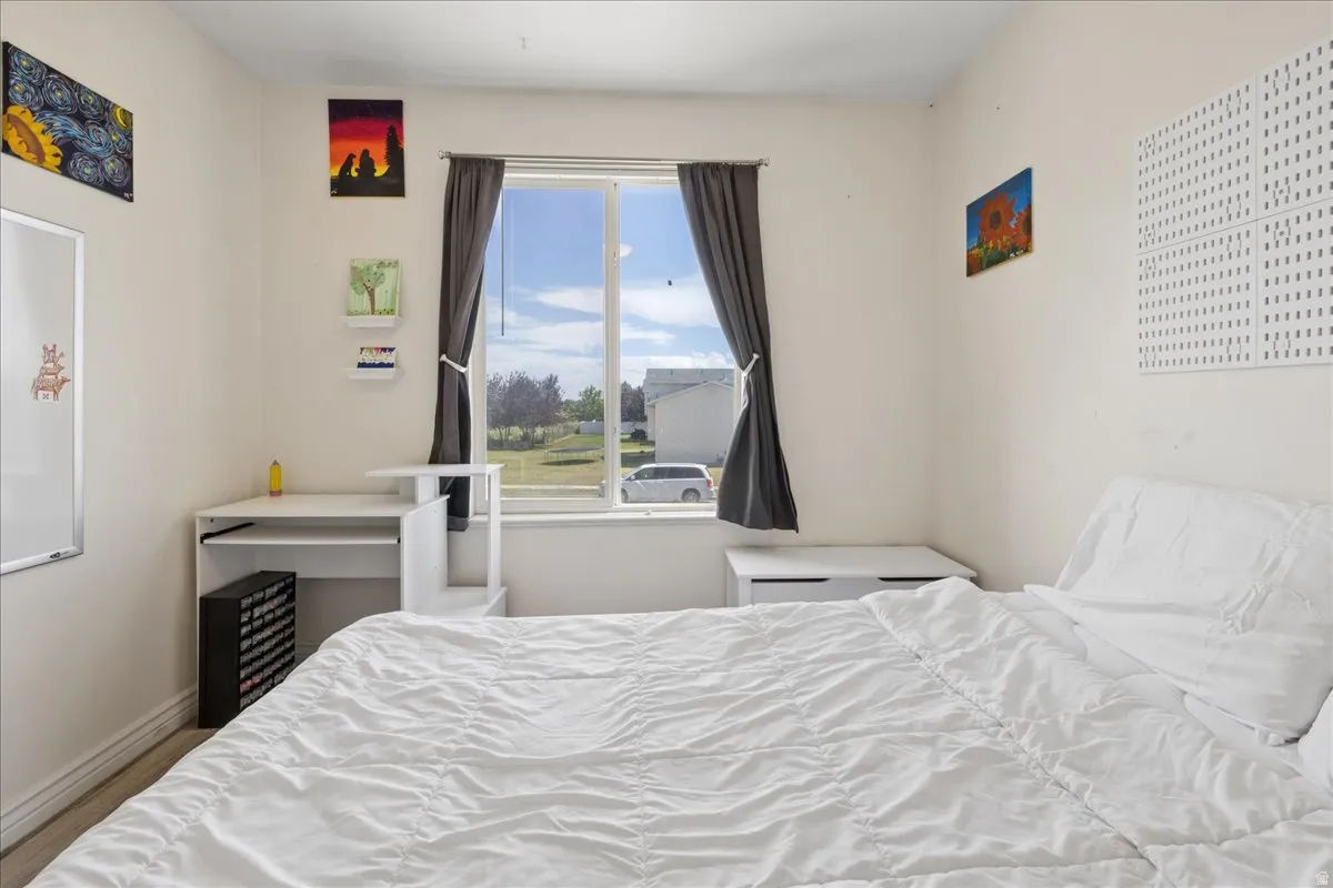 Bright interior space featuring a window with dark drapes, light-colored walls, and wood-finish flooring