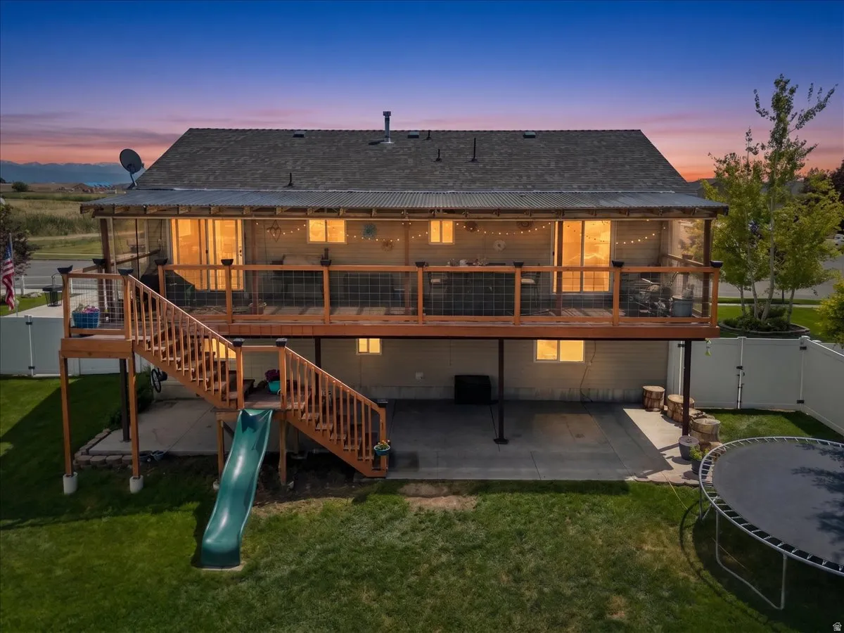 Spacious rear exterior featuring a substantial elevated deck with staircase, ground-level concrete patio, mature green lawn, and full privacy fencing