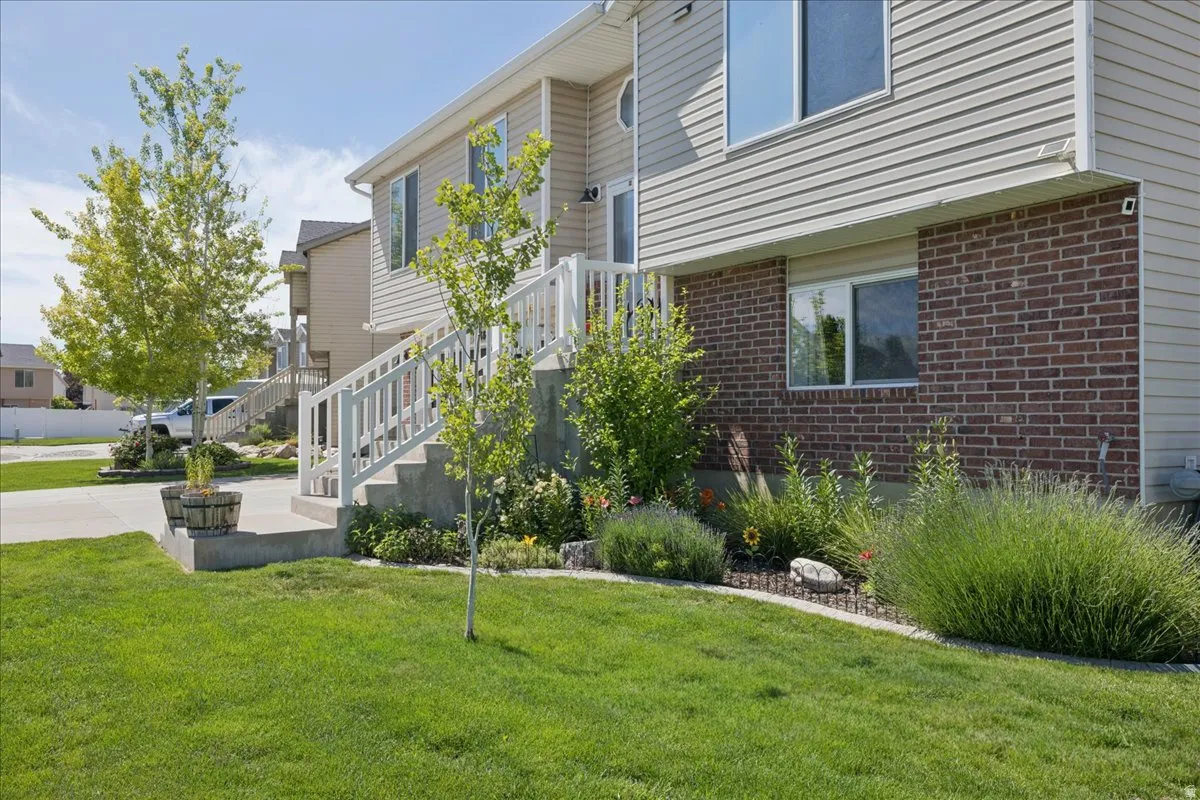 Exterior featuring a combination of brick and siding, concrete steps with white railings, a landscaped garden bed, a manicured lawn, and mature trees