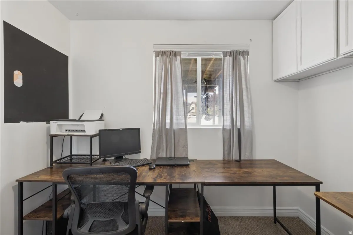 Dedicated office space featuring a window with natural light, wall-mounted cabinetry, and a textured carpeted floor
