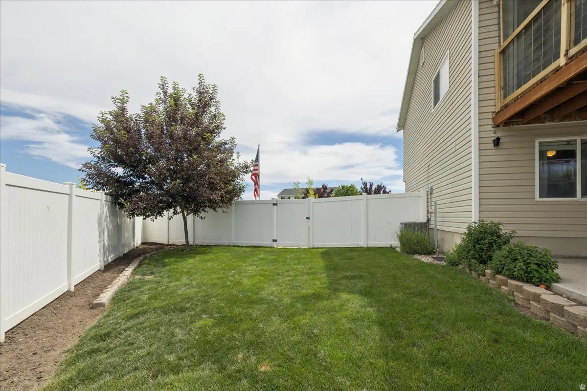 Expansive rear yard featuring a manicured lawn, full privacy fencing, and a mature shade tree