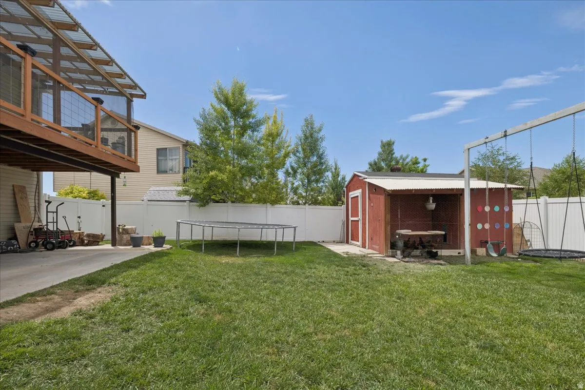 Expansive green lawn featuring a red utility shed with an open-sided extension, a swing set, and a two-story wood deck with a translucent roof cover