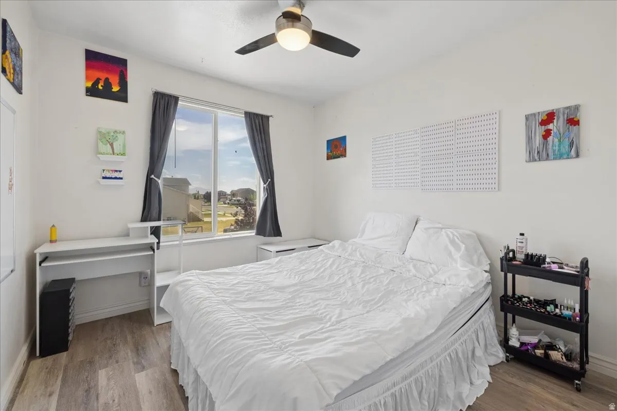 Bedroom featuring wood-finish flooring, a ceiling fan with integrated lighting, and a large window with privacy coverings