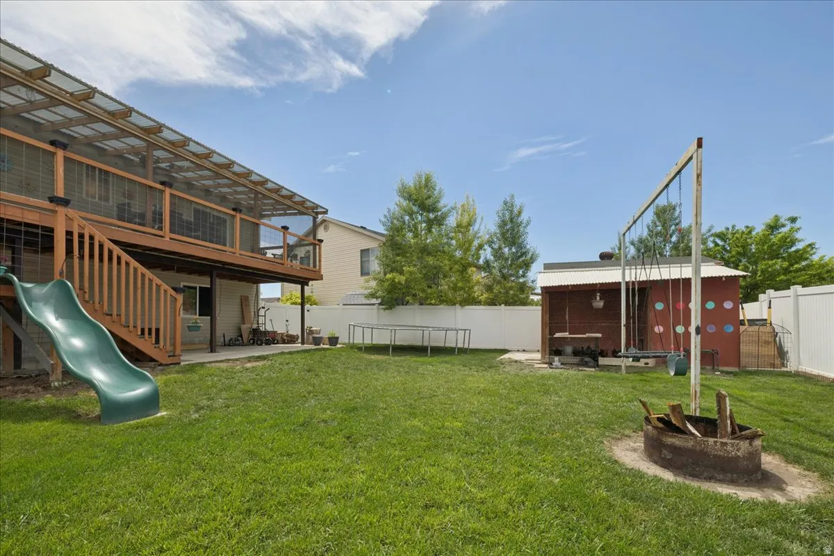Expansive backyard featuring a covered upper deck with wood railing, a lower concrete patio, and a built-in fire pit