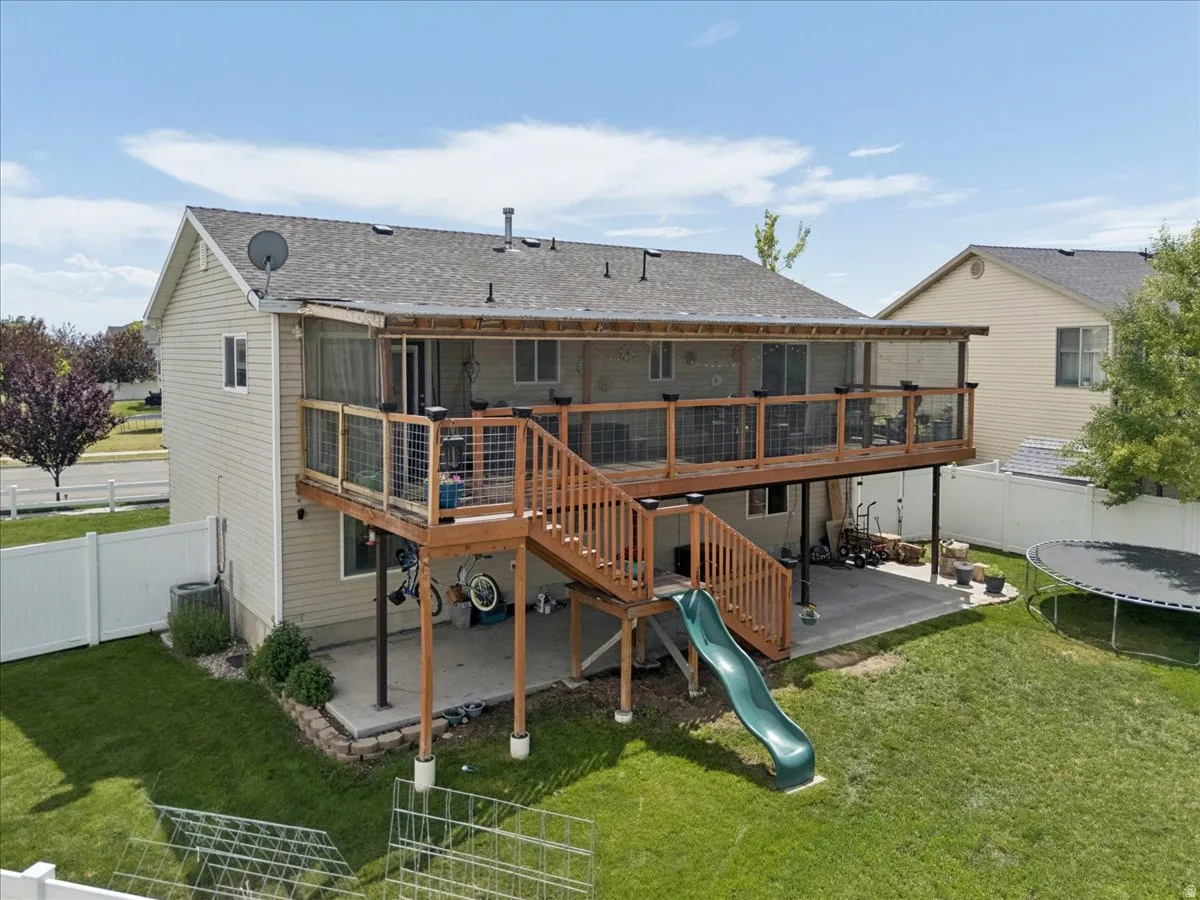 Rear exterior featuring a screened-in deck with wood railing and stairs, a lower concrete patio, and a fenced yard with established landscaping