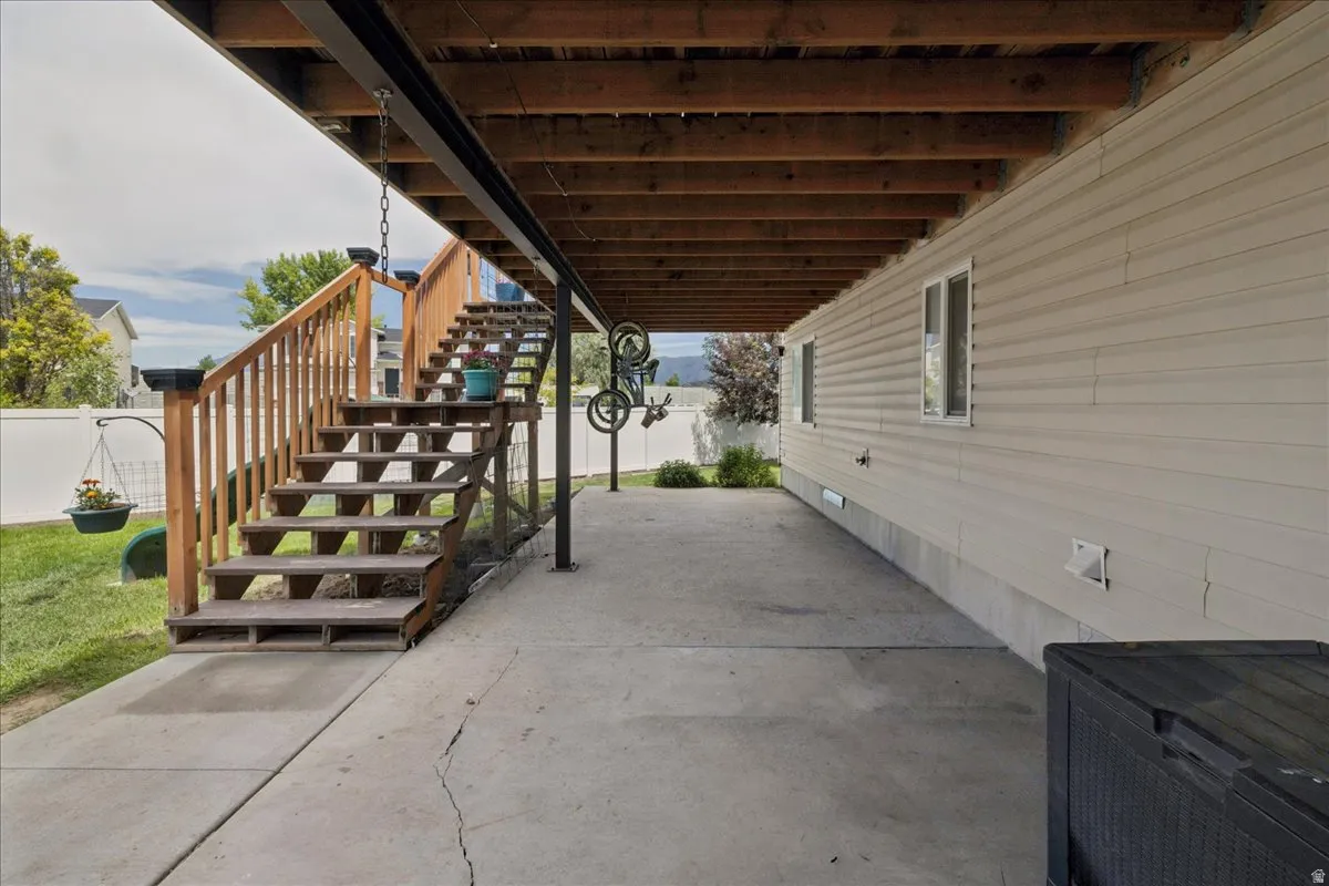 Covered concrete patio with exposed wood joist ceiling, wood staircase, and vinyl siding