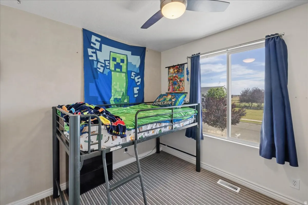 Bedroom featuring a window with exterior views, striped carpet, a ceiling fan with integrated lighting, and white baseboards