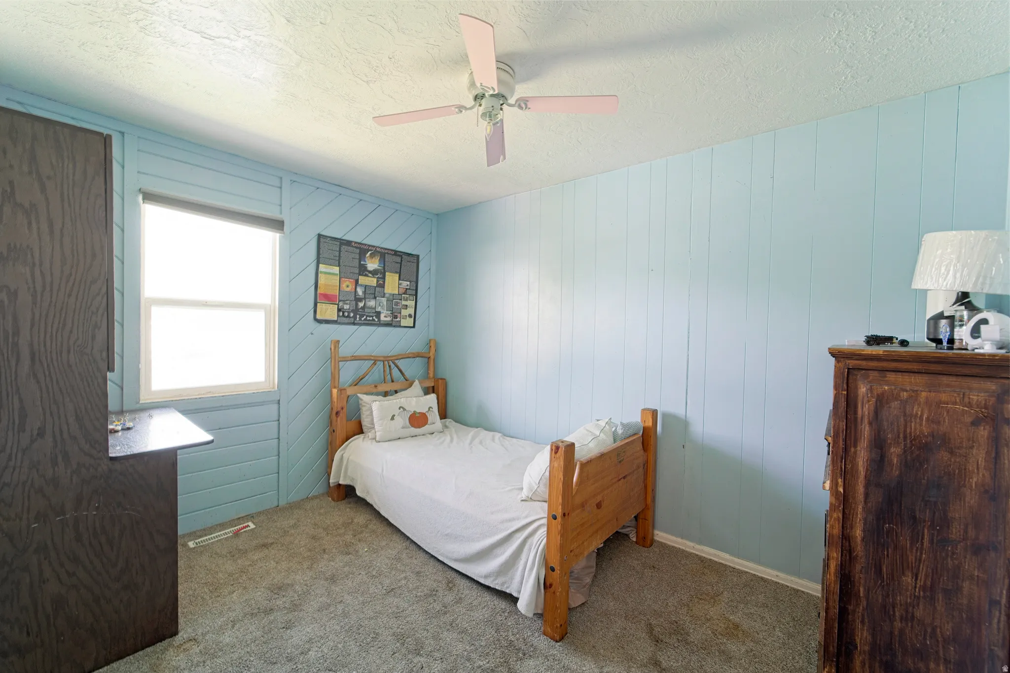 Bedroom featuring light blue wood paneling, a ceiling fan, white trim, and a window with a roller shade