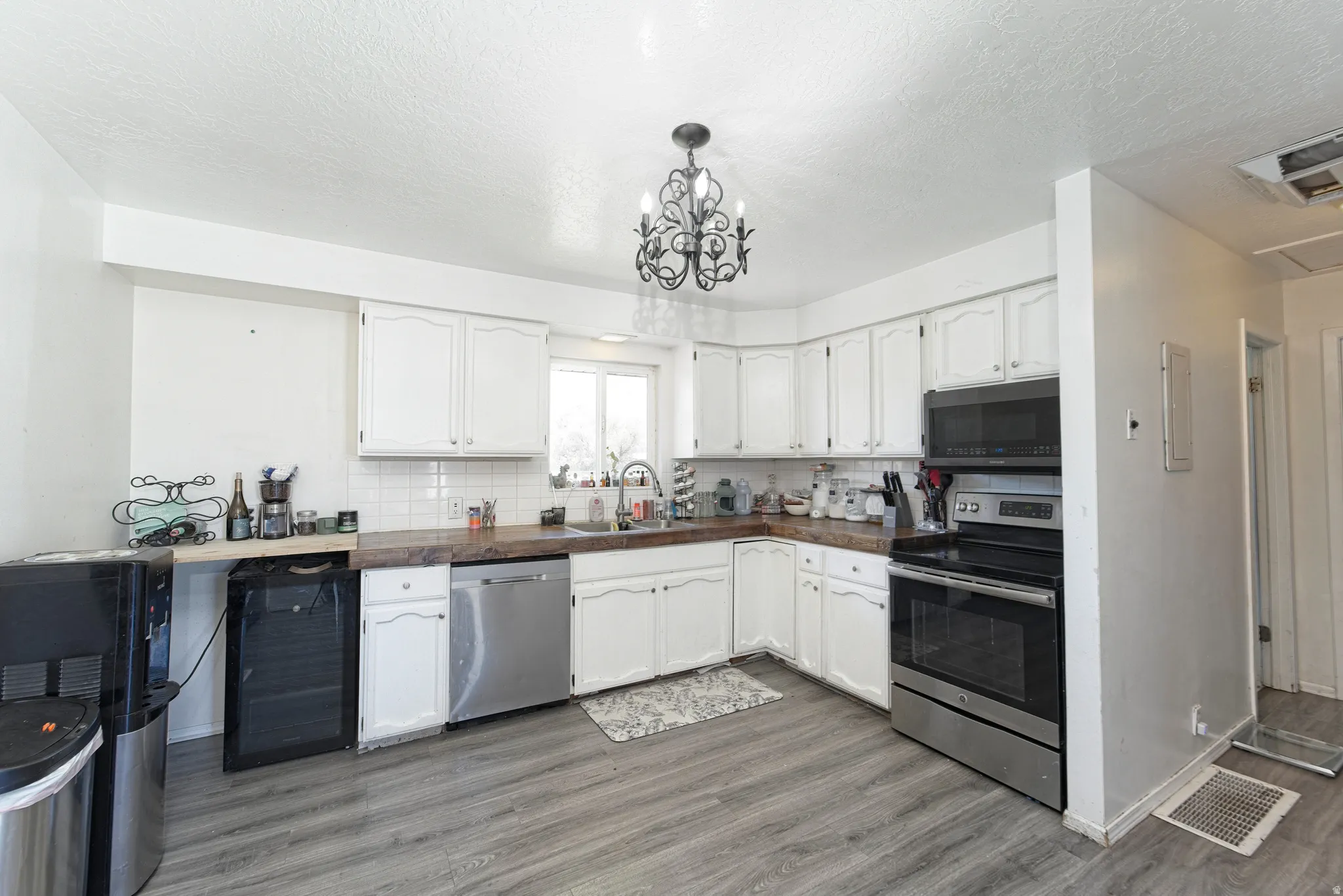 Kitchen featuring white cabinetry, gray wood-finish flooring, a stainless steel dishwasher, a stainless steel range with overhead microwave, and a decorative overhead light fixture