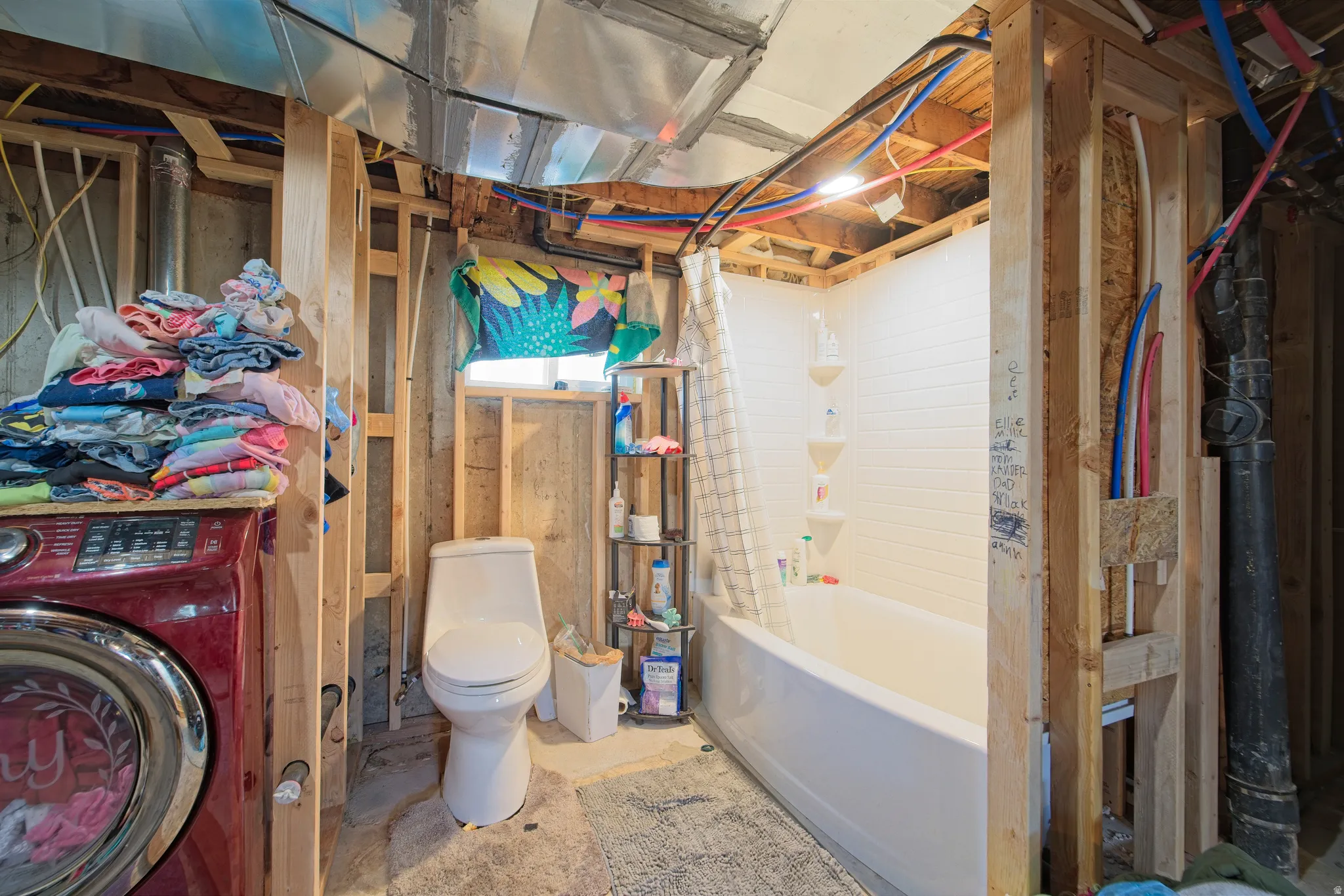 Partial bathroom featuring a white bathtub with subway tile surround, white toilet, and exposed wood framing