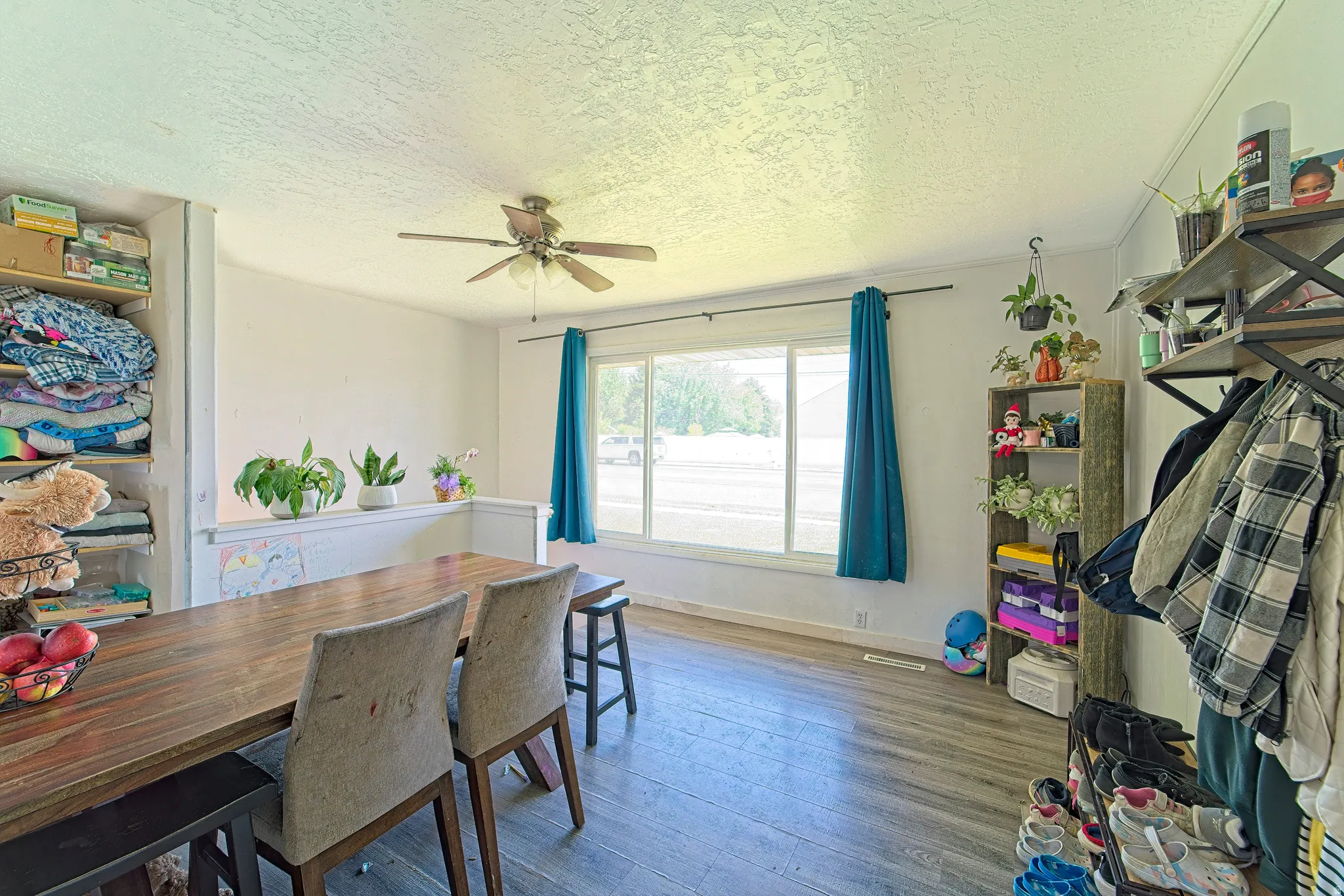 Spacious interior room featuring wood-finish flooring, a ceiling fan, and large windows with blue drapery