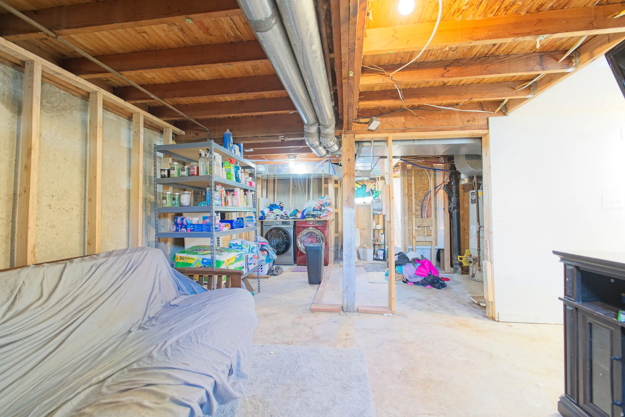Unfinished basement featuring exposed wood joists, concrete foundation walls, and visible ductwork