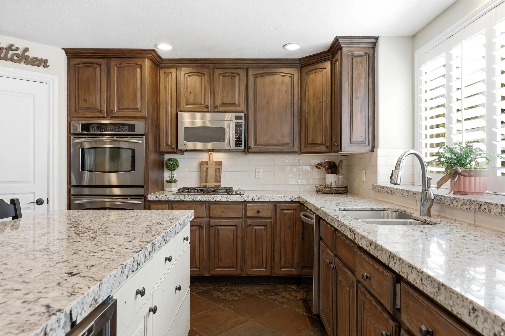 Kitchen featuring custom cabinetry, light-toned granite countertops, stainless steel appliances, and subway tile backsplash