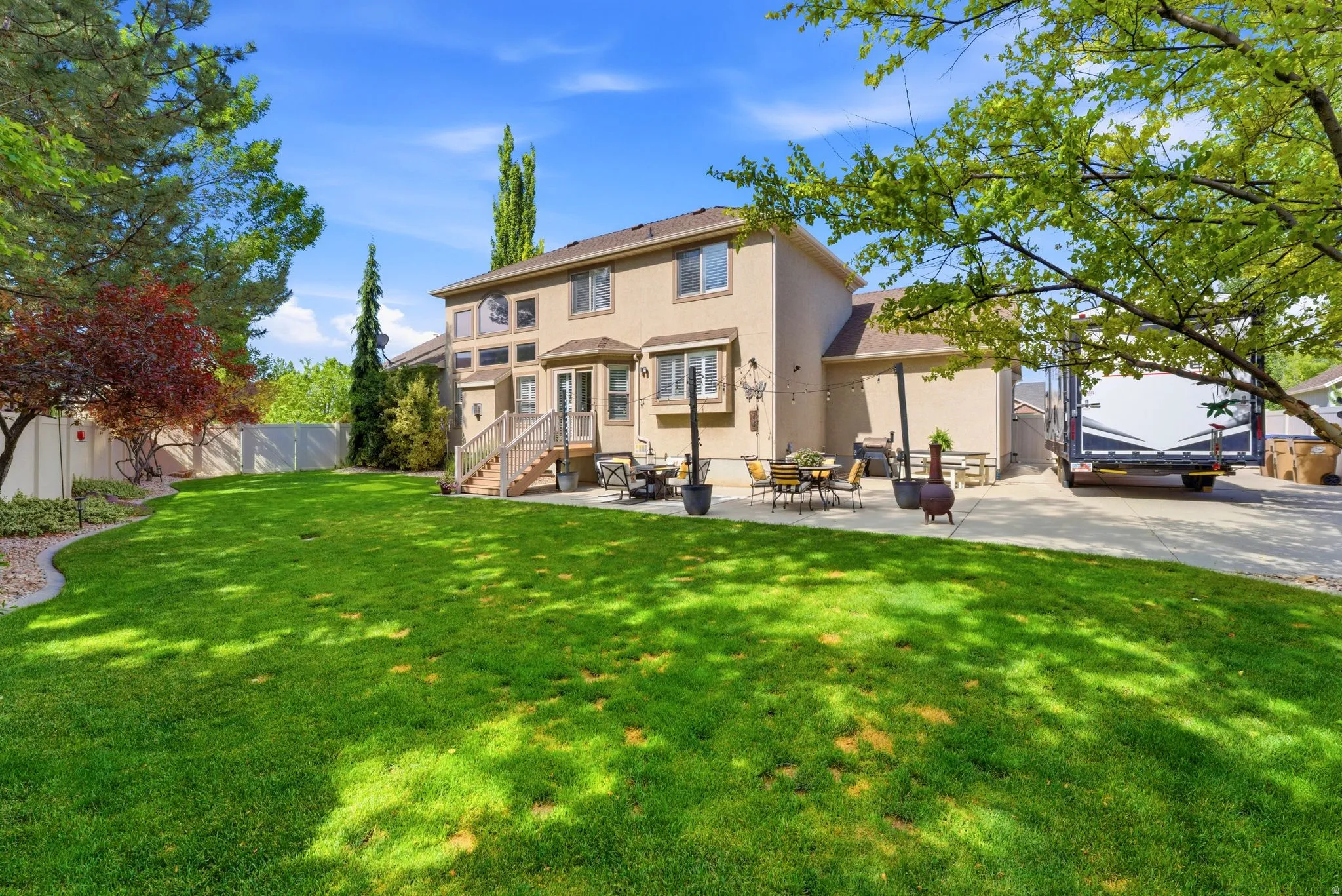 Expansive backyard featuring a lush lawn, mature trees, and a spacious patio area