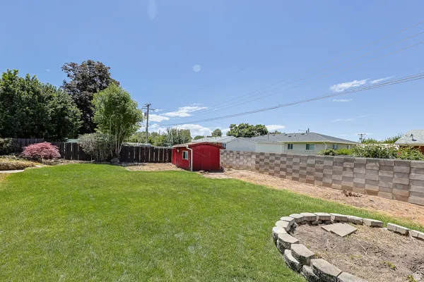 Expansive lawn area featuring a red utility shed, a decorative stone fire pit, and a segmented block retaining wall