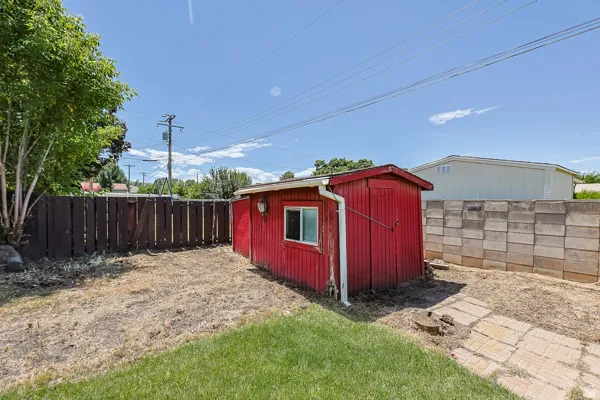 Red utility shed with a window, positioned on a grassy lot