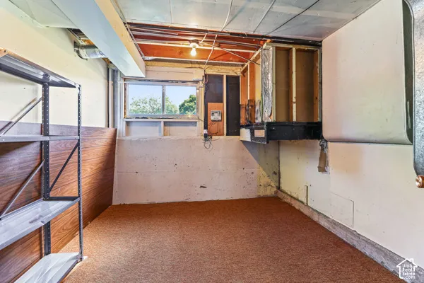Basement space featuring a window, exposed ceiling joists, and a partial wood-finish wall