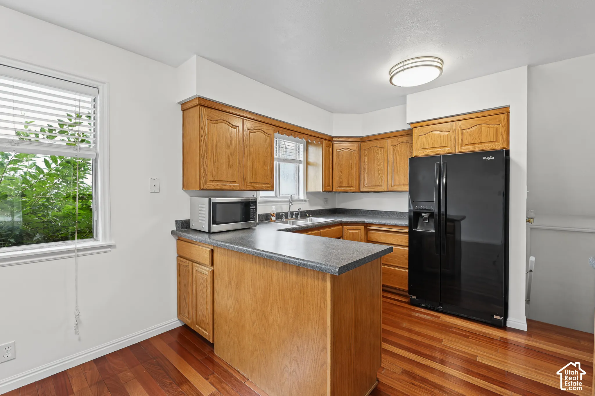 Kitchen featuring wood-finish flooring, wood cabinetry, dark countertops, and a black refrigerator