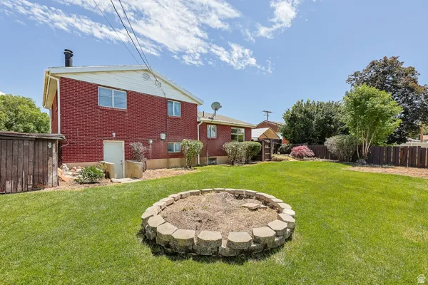 Expansive green lawn featuring a stone-edged fire pit, a red brick exterior, and a wooden privacy fence