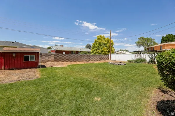 Expansive backyard featuring a manicured lawn, a red storage shed with a single window, and a decorative block wall