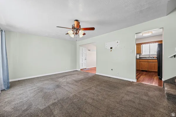 Spacious room featuring gray wall-to-wall carpeting, a ceiling fan with integrated lighting, and light-toned walls