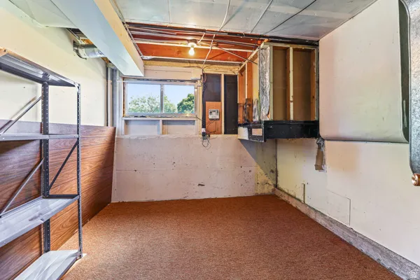Basement space featuring a window, exposed ceiling joists, and a partial wood-finish wall
