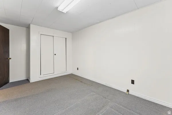 Room featuring light gray carpet, white painted walls, white trim, a built-in closet with sliding doors, and an overhead fluorescent light fixture
