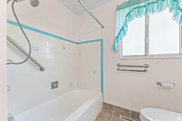 Full bathroom featuring a white porcelain tub, white tiled shower surround with blue accent trim and floral details, and a chrome showerhead with a flexible hose