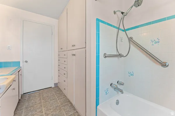 White tiled shower with turquoise trim, a handheld showerhead, and grab bars