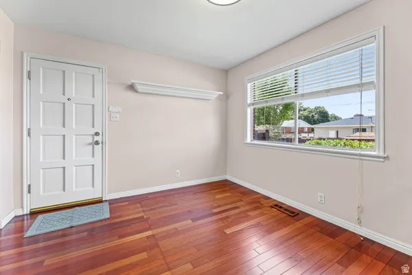 Spacious room featuring wood-finish flooring, a paneled entry door, and a large window with blinds