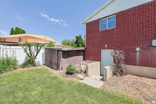 Brick exterior featuring a basement entry, a white vinyl fence, and a storage shed