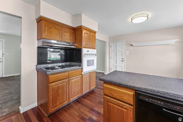 Kitchen featuring wood cabinetry, dark countertops, a built-in oven, and a cooktop with an overhead range hood