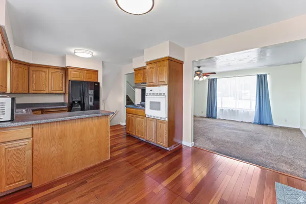 Kitchen featuring wood-finish flooring, oak cabinetry, black appliances, light-toned countertops, and a built-in oven