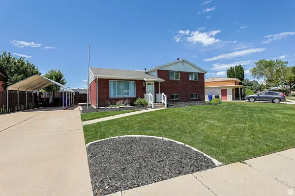 Brick-front residence featuring a covered carport, concrete driveway, and a front yard with manicured lawn and decorative landscaping