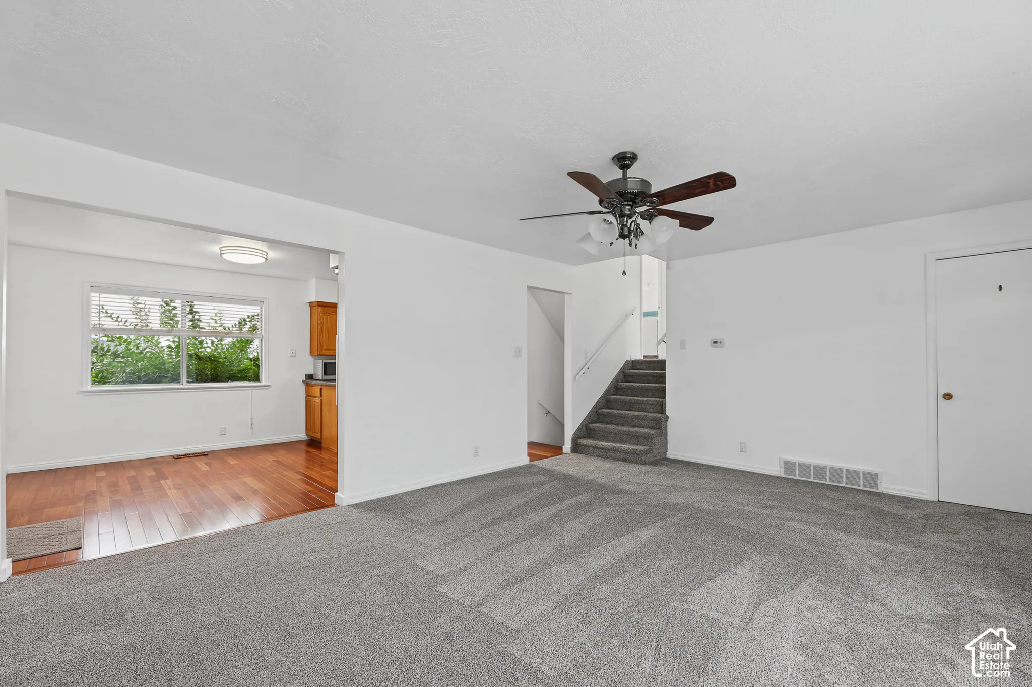 Carpeted living area with a ceiling fan, staircase, and white walls