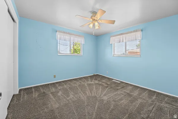 Room featuring two windows with horizontal blinds, a ceiling fan, and grey patterned carpeting