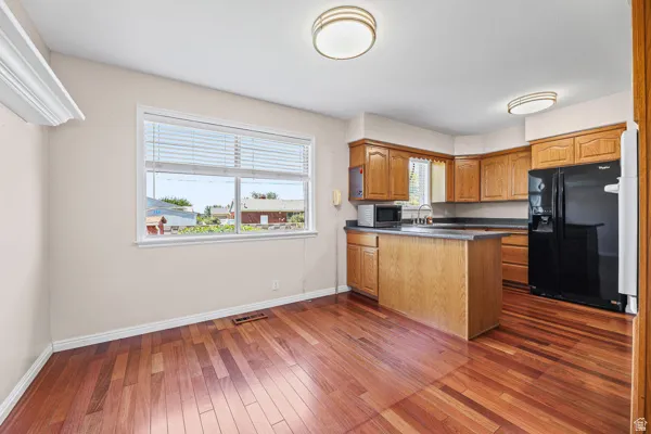 Open-concept kitchen and dining area featuring wood-finish flooring, a kitchen island with dark countertops, oak cabinetry, and a double-pane window with blinds