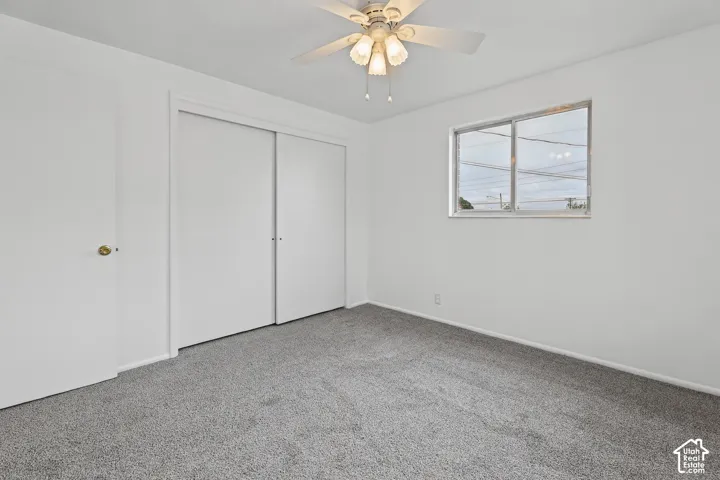 Bedroom 2 Neutral tone walls, grey carpet flooring, sliding closet doors, window with horizontal panes, and a ceiling fan with light fixture