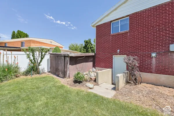 Brick exterior featuring a basement entry, a white vinyl fence, and a storage shed