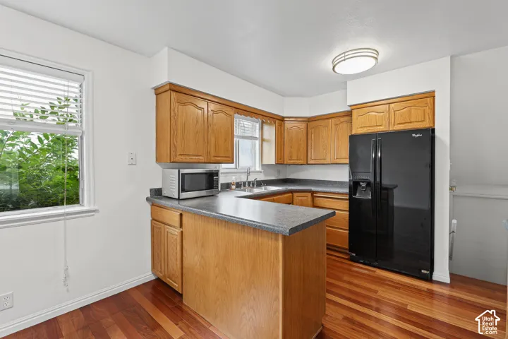 Kitchen featuring wood-finish flooring, wood cabinetry, dark countertops, and a black refrigerator