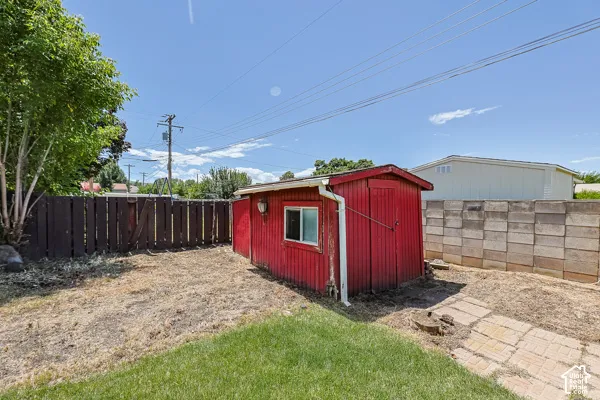 Red utility shed with a window, positioned on a grassy lot