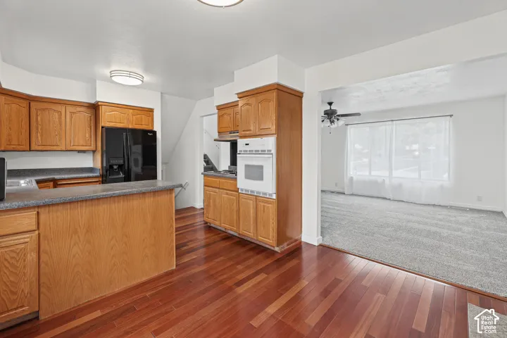 Wood-finish flooring, wood cabinetry, built-in oven, black refrigerator, and an arched opening to a carpeted living area