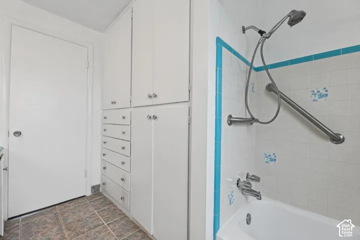 White built-in cabinetry with multiple drawers and cabinet doors, tiled flooring, white bathtub with wall-mounted showerhead, and a grab bar