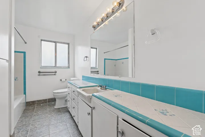 Bathroom featuring a ceramic tile floor, white vanity with integrated sink, tiled countertop with accent trim, and a window for natural light